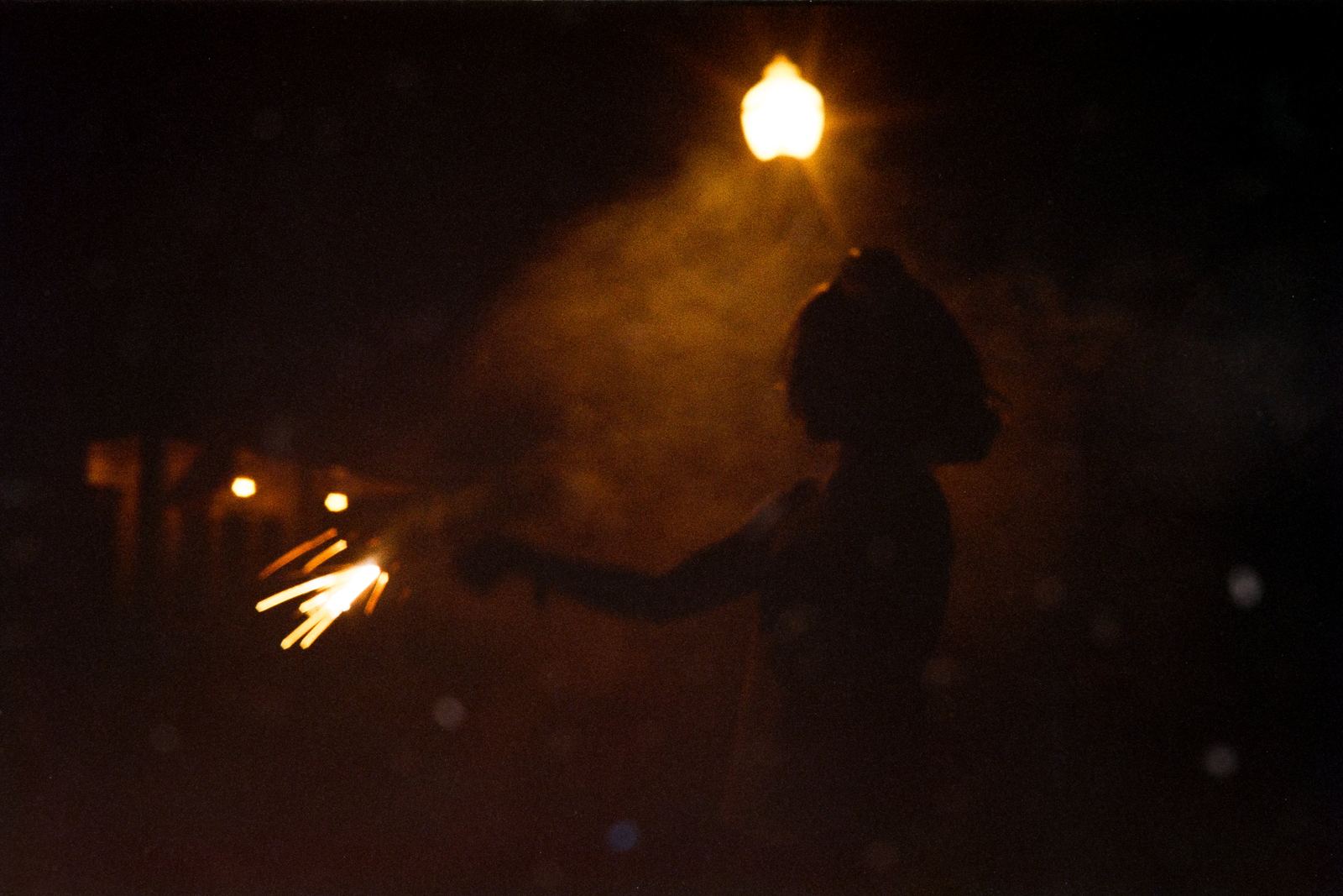 A silhouetted figure holding a sparkler beneath a streetlight